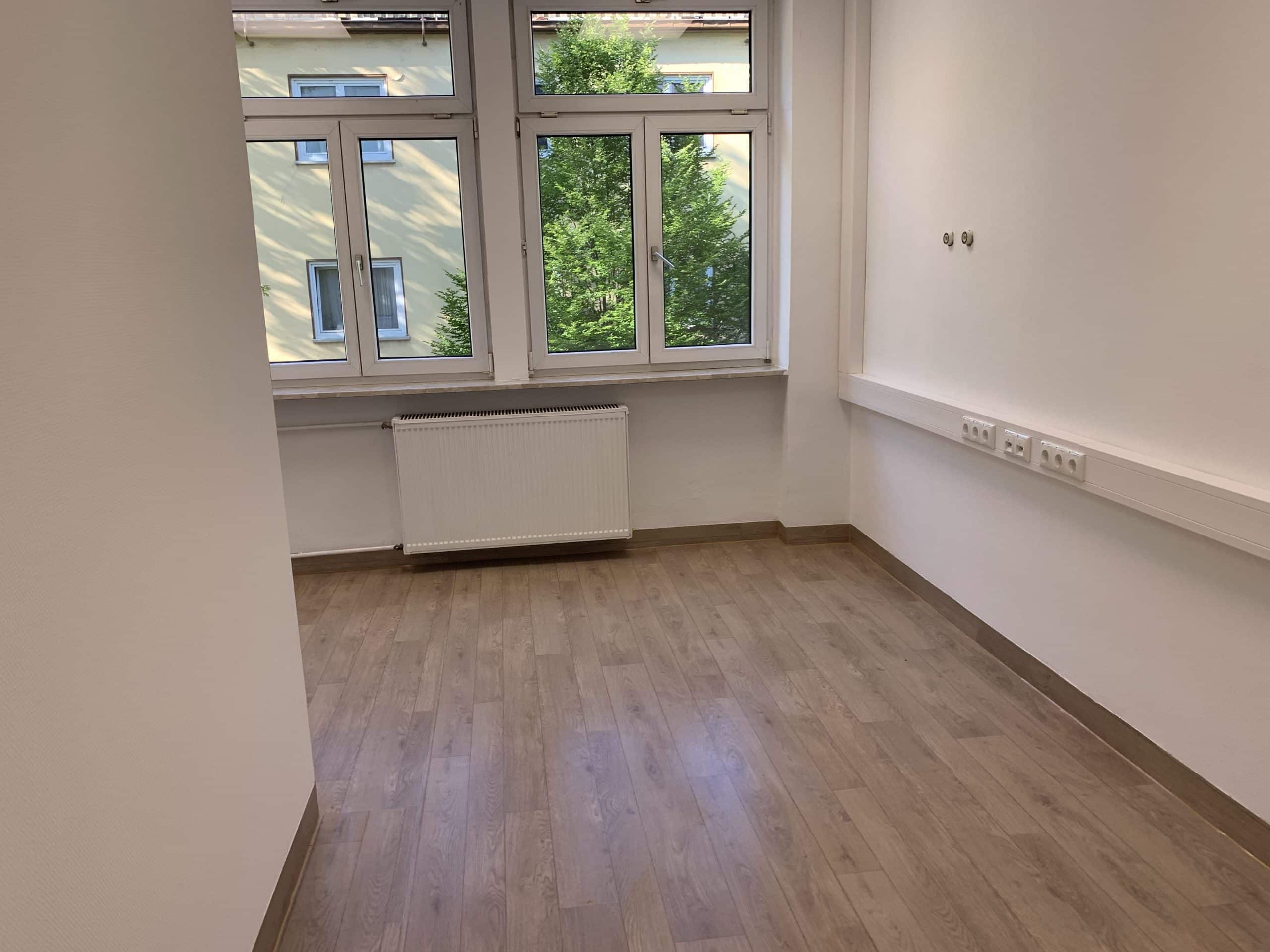 Ein lichtdurchfluteter Raum mit weißen Wänden, Fenstern und Steckdosen. Dazu ist ein weißer Heizkörper unter den Fenstern befestigt.